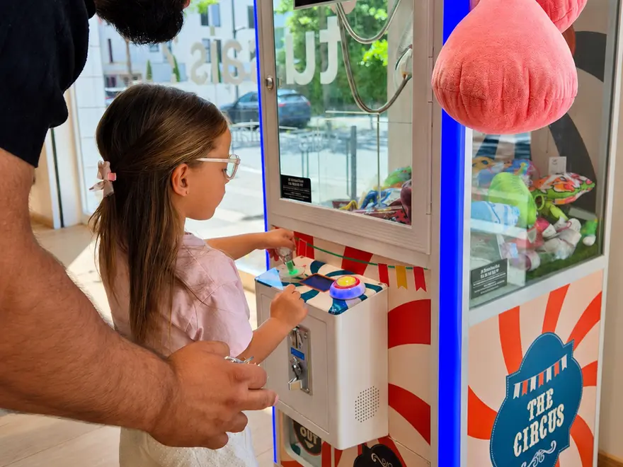 Une fillette joue à la machine à pinces du magasin, accompagnée de son papa.