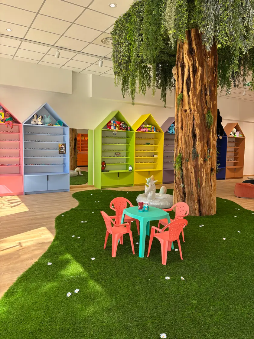 Le pied de l'arbre et la petite table entourée de chaises corail, sur la pelouse de l'espace enfant.